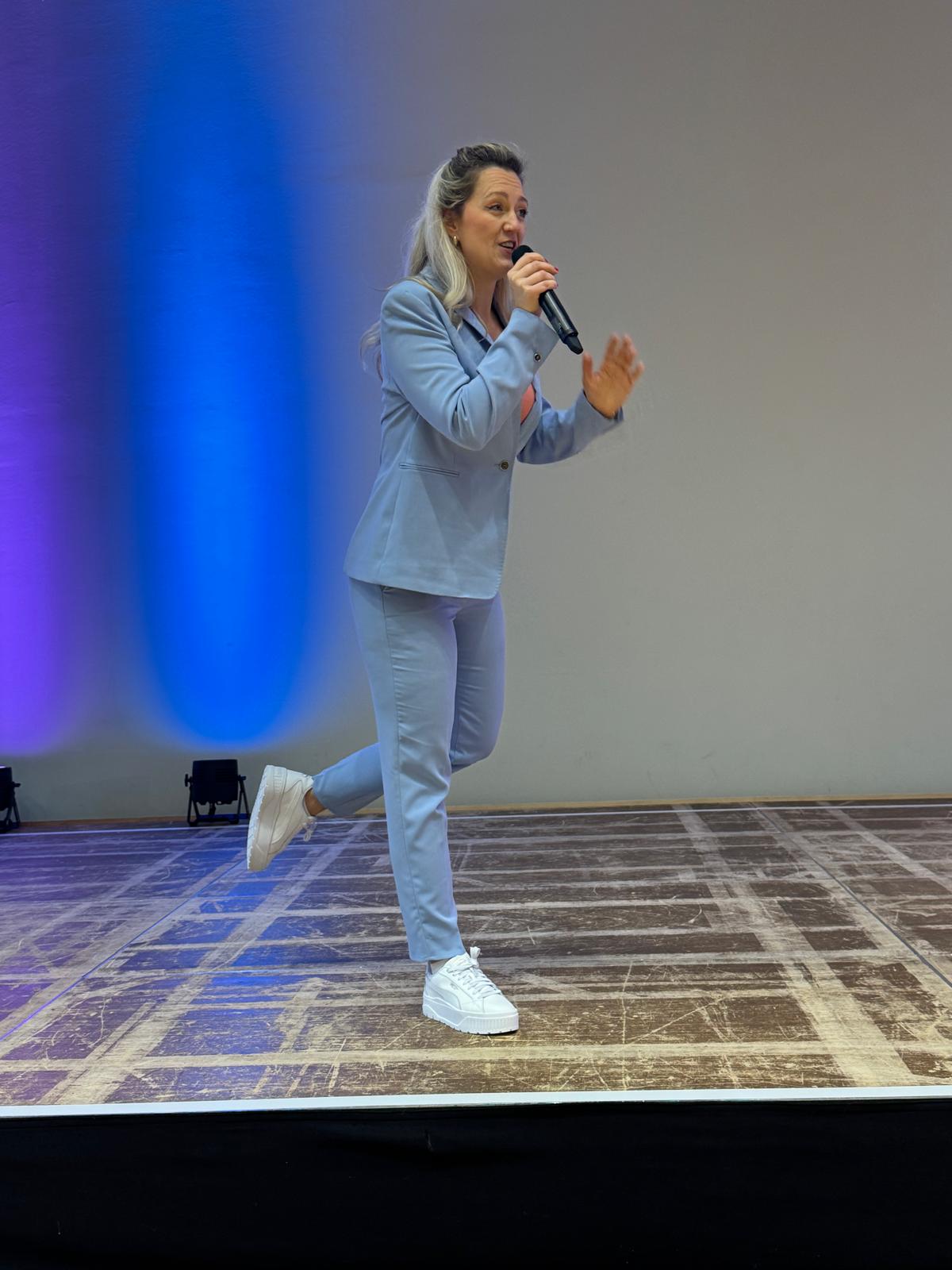 Hanna Czarnecka moderiert im hellblauen Anzug auf der Bühne der Kinder-Eventwelt